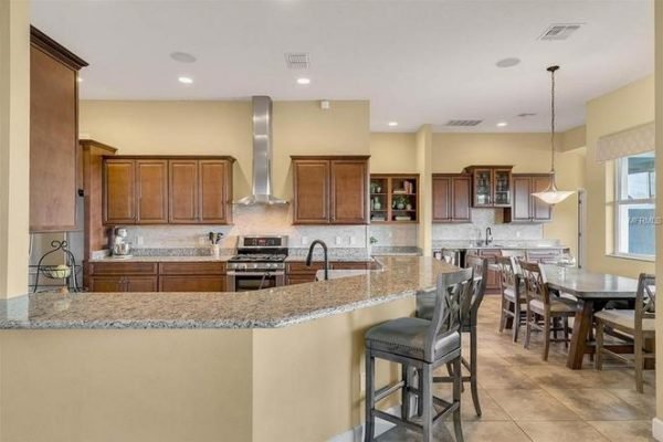 Modern kitchen in Winter Garden, featuring granite countertops, wooden cabinetry, stainless steel appliances, and a dining area with a large table, showcasing spacious layout and elegant design.