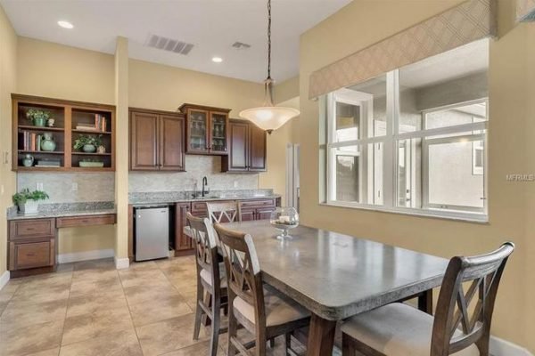 Modern kitchen and dining area in Winter Garden home, featuring wooden cabinetry, stainless steel appliances, and a large dining table, highlighting spaciousness and natural light.