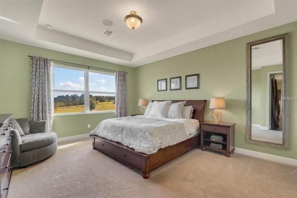 Spacious master bedroom in Winter Garden, featuring a king-sized bed, decorative wall art, large windows with scenic views, and cozy sitting area with a gray chair.