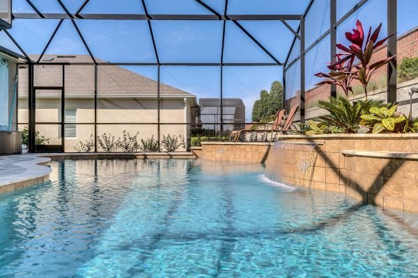 Sleek saltwater pool with waterfall feature and screen enclosure, surrounded by tropical landscaping in Winter Garden, FL home at 15390 Sandfield Loop.