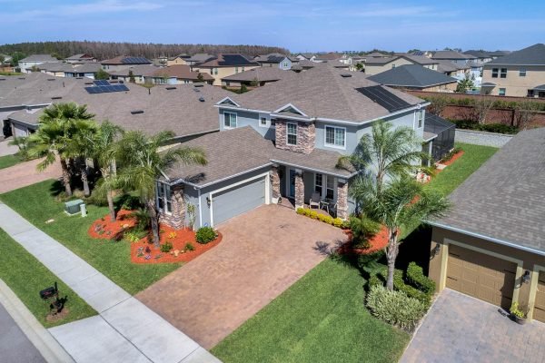 Aerial view of 15390 Sandfield Loop, Winter Garden, FL, showcasing a modern home with stone accents, a brick paver driveway, and lush landscaping, part of the gated Reserve at Carriage Pointe community.