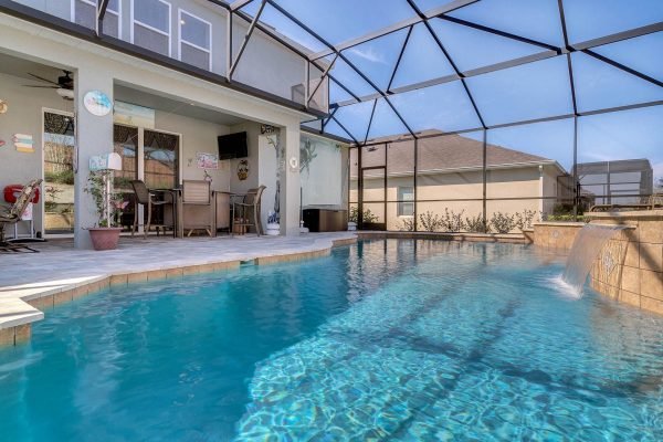 Saltwater pool with waterfall feature and covered lanai in backyard of 15390 Sandfield Loop, Winter Garden, FL, showcasing outdoor living space and Florida sunshine.