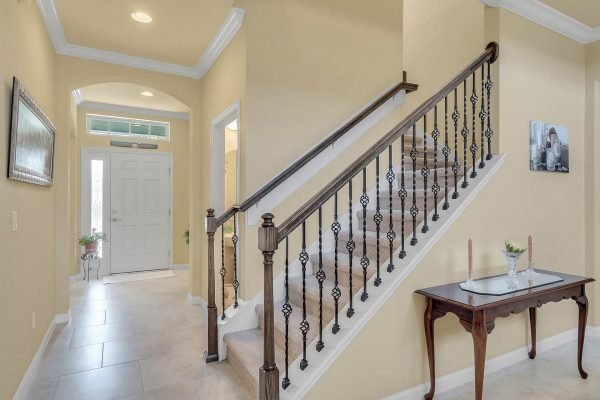 Foyer entrance of 15390 Sandfield Loop in Winter Garden, featuring a staircase with wrought iron railing, tiled flooring, and natural light from the front door.