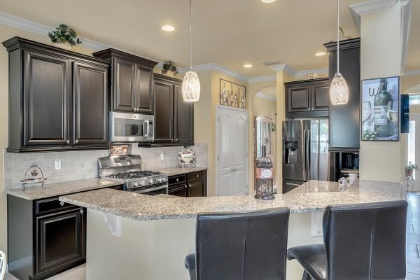 Modern kitchen with dark wood cabinetry, granite countertops, stainless steel appliances, and pendant lighting, showcasing a spacious layout ideal for entertaining in the Winter Garden home at 15390 Sandfield Loop.
