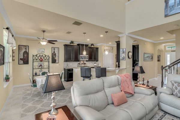 Spacious family room featuring modern furnishings, light-colored walls, and an open layout connecting to the kitchen, showcasing dark cabinetry and dining area, ideal for entertaining in the Hillsdale floor plan home at 15390 Sandfield Loop, Winter Garden, FL.