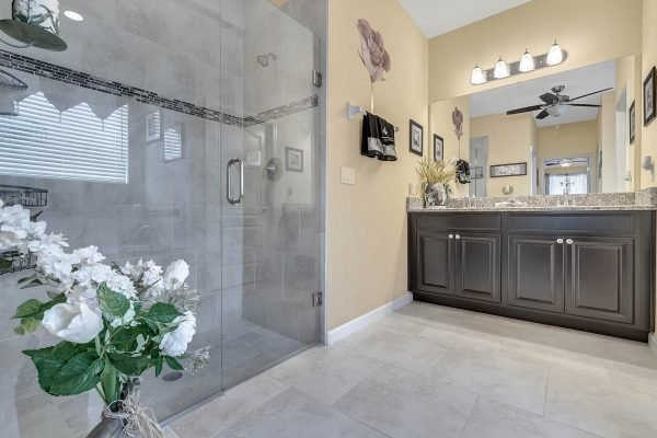 Master bathroom featuring a glass shower, dark cabinetry, granite countertops, and decorative floral accents in a home at 15390 Sandfield Loop, Winter Garden, FL.