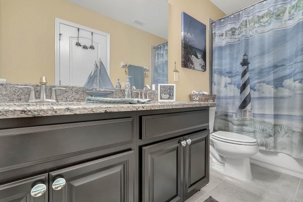 Bathroom featuring dark cabinetry, granite countertop, and nautical-themed shower curtain with a lighthouse design, highlighting a clean and inviting space in the home at 15390 Sandfield Loop, Winter Garden, FL.