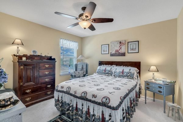 Cozy bedroom featuring a queen-sized bed with nautical-themed bedding, wooden dresser, bedside lamps, and decorative wall art, showcasing a warm and inviting atmosphere in the Winter Garden home at 15390 Sandfield Loop.
