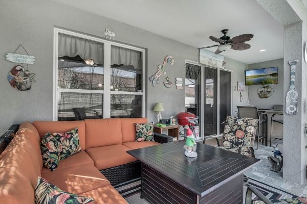 Covered lanai with tropical-themed seating, coffee table, and decorative accents, showcasing a cozy outdoor living space in Winter Garden, FL home at 15390 Sandfield Loop.