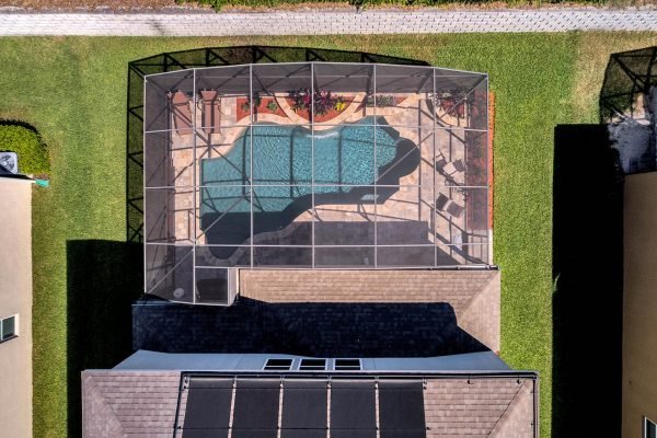 Aerial view of a landscaped backyard featuring a screened saltwater pool, surrounded by patio furniture and lush greenery, located at 15390 Sandfield Loop, Winter Garden, FL.