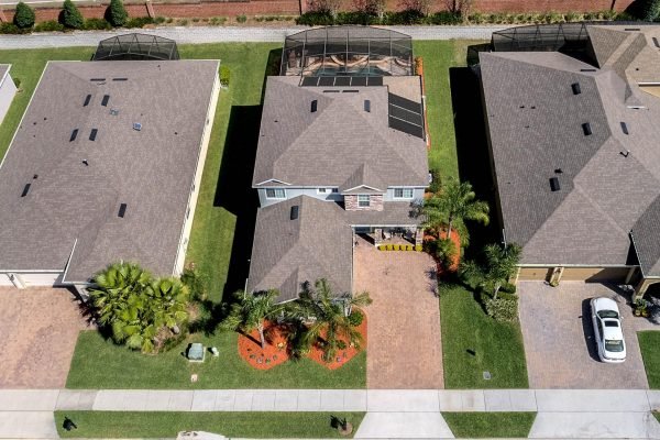 Aerial view of 15390 Sandfield Loop in Winter Garden, FL, showcasing a spacious 4-bedroom home with a brick paver driveway, surrounded by well-maintained lawns and palm trees, featuring a screened pool enclosure in the backyard.