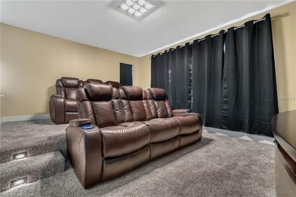 Home theater room featuring plush brown recliners, dark curtains, and soft carpet, highlighting the luxurious upgrades of the Windermere property at 9007 Outlook Rock Trl.
