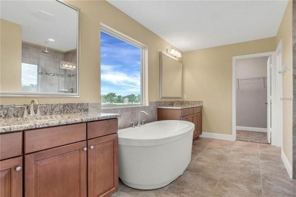 Luxurious bathroom featuring a freestanding tub, dual vanities with granite countertops, large windows providing natural light, and elegant tile flooring, located in a Windermere home for sale.