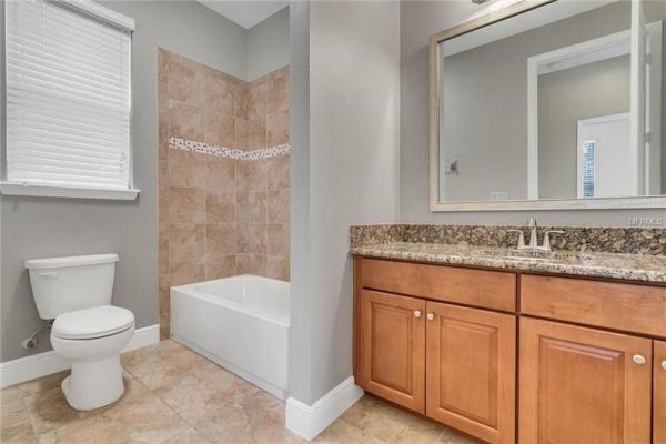 Modern bathroom with beige tile shower, white bathtub, and wooden cabinetry, showcasing upgraded features and spacious layout in Windermere, FL home.