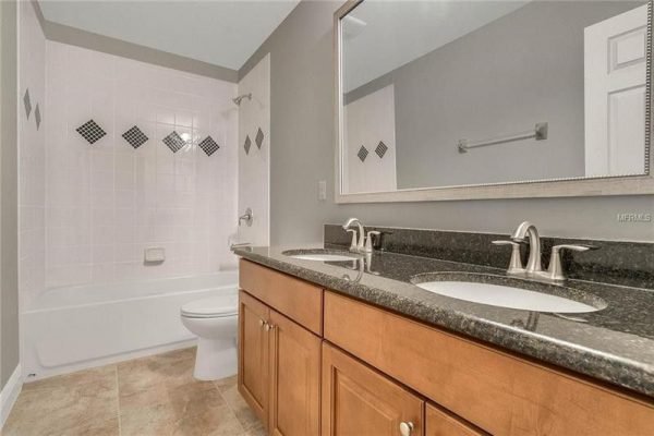 Modern bathroom featuring dual sinks with granite countertops, a bathtub with tiled surround, and decorative accents, designed for the upgraded Windermere home at 9007 Outlook Rock Trail.