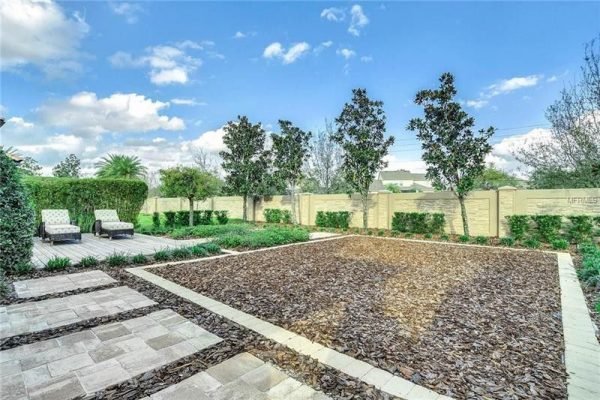 Backyard of 9007 Outlook Rock Trail, Windermere, FL, featuring landscaped area with decorative stone, lush greenery, and lounge chairs, highlighting outdoor living space.