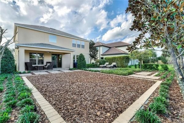 Backyard view of 9007 Outlook Rock Trail, Windermere, FL, featuring landscaped area with mulch, seating area, and neighboring homes, highlighting outdoor living space and community appeal.