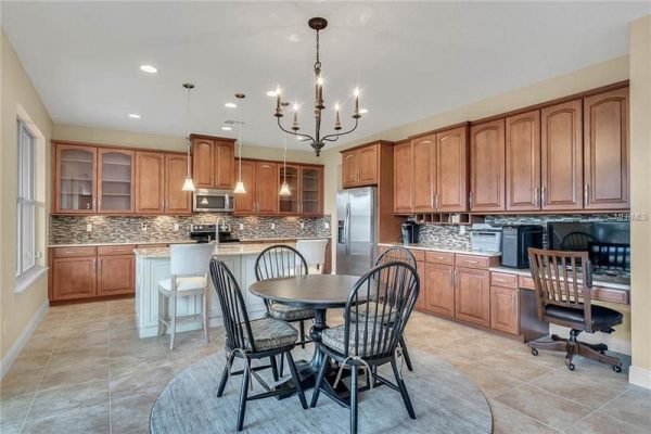 Modern kitchen in Windermere, FL, featuring wooden cabinetry, stainless steel appliances, and a round dining table with black chairs, highlighting an open floor plan and stylish design.