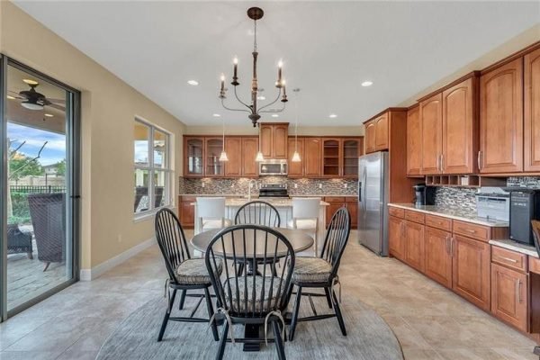 Modern kitchen with wood cabinetry, stainless steel appliances, and a round dining table, showcasing an open layout and natural light from large windows in Windermere, FL home.