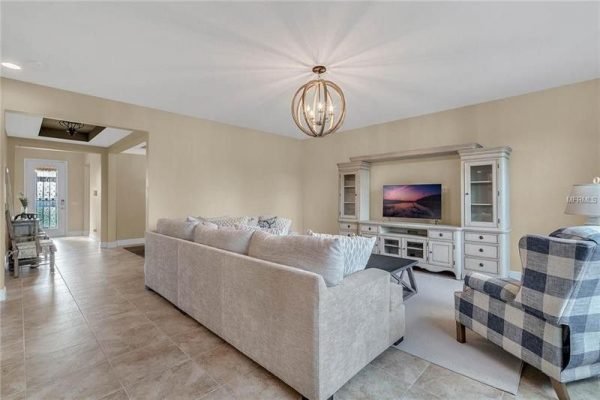 Spacious living room featuring a light-colored sectional sofa, a modern entertainment unit with a TV, and a stylish accent chair, illuminated by a decorative pendant light, showcasing the inviting interior of a Windermere home at 9007 Outlook Rock Trail.