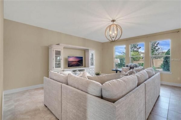Spacious living room with a modern sectional sofa, elegant light fixture, and large windows showcasing outdoor views, highlighting the upgraded interior of 9007 Outlook Rock Trail in Windermere, FL.