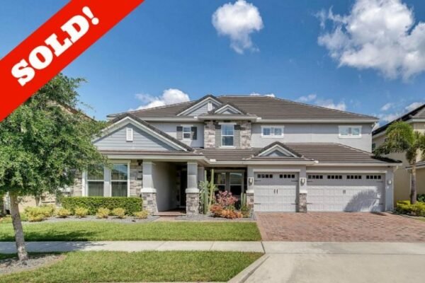 Sold sign on a spacious two-story home with a stone-accented facade, featuring a three-car garage, manicured lawn, and clear blue sky in Windermere, FL.