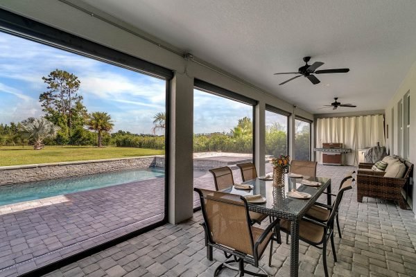 Screened-in patio with dining table, pool view, and lush greenery in Windermere, Florida, showcasing outdoor living space ideal for entertaining.