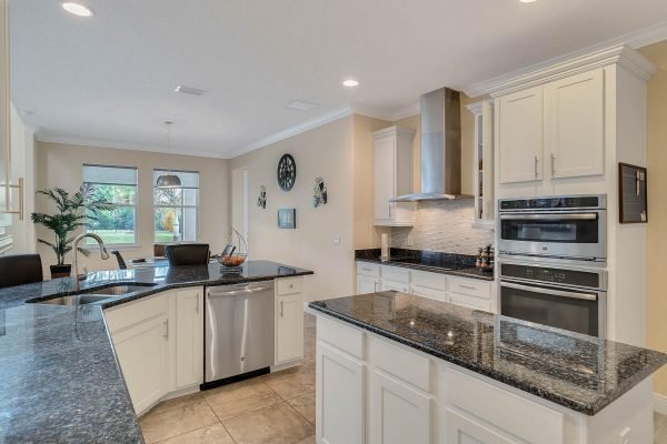 Modern kitchen with granite countertops, white cabinetry, stainless steel appliances, and large windows providing natural light, showcasing the spacious layout of the home at 11637 Brickyard Pond Lane, Windermere, FL.