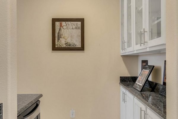 Wine cellar sign on wall in elegant kitchen space with granite countertops and white cabinetry.