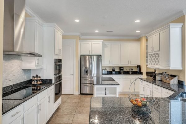 Modern kitchen with white cabinetry, granite countertops, stainless steel appliances, and an island, showcasing a spacious layout ideal for a luxury home in Windermere, FL.
