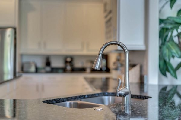 Modern kitchen faucet with stainless steel finish, granite countertop, and blurred background of a spacious kitchen setting in Windermere, FL.