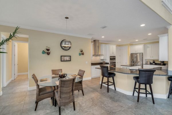Modern kitchen and dining area in Windermere home featuring a round table with wicker chairs, stainless steel appliances, and a spacious layout with light-colored walls and tile flooring.