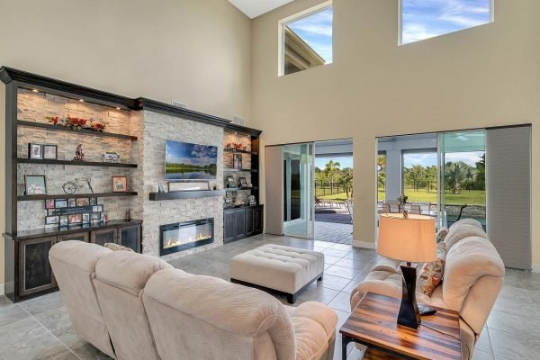 Spacious family room featuring a modern stone fireplace, built-in shelves, large windows with views of the outdoor area, and comfortable seating, located in a lakefront estate at 11637 Brickyard Pond Lane, Windermere, FL.