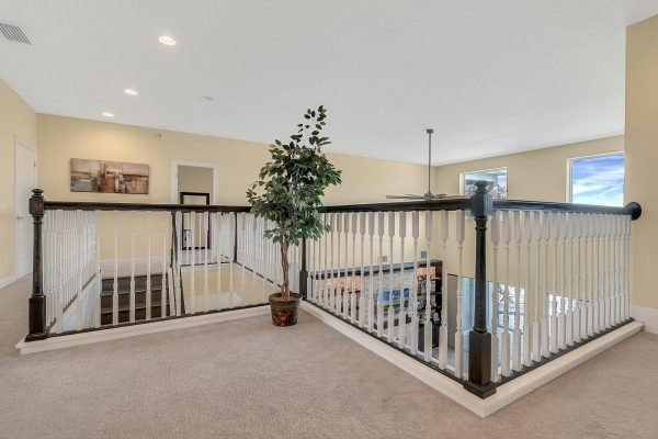 Spacious loft area with decorative railings, potted plant, and large windows, showcasing a bright and airy atmosphere in a Windermere, FL home.