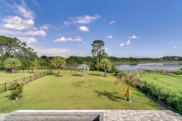Lakefront view from 11637 Brickyard Pond Lane, Windermere, showcasing expansive green lawn, palm trees, and serene water landscape under a clear blue sky.