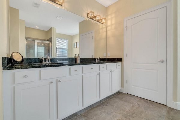 Master bathroom featuring a spacious double vanity with white cabinetry, dark granite countertop, modern fixtures, and natural light from nearby windows.
