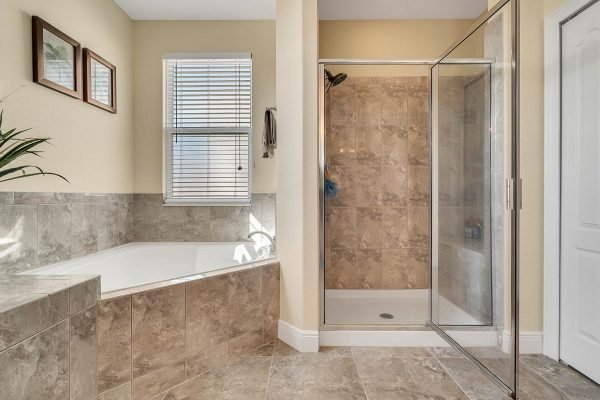 Master bathroom featuring a spacious layout with a soaking tub, glass-enclosed shower, and natural light from windows, showcasing modern tile design and fixtures in a Windermere estate.