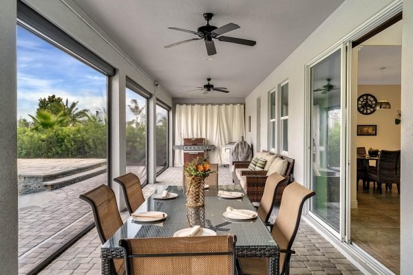 Lanai dining area with table set for six, featuring a centerpiece of flowers, overlooking a spacious backyard with outdoor grill and views of lush greenery, emphasizing the luxurious outdoor living space of the Windermere estate at 11637 Brickyard Pond Lane.