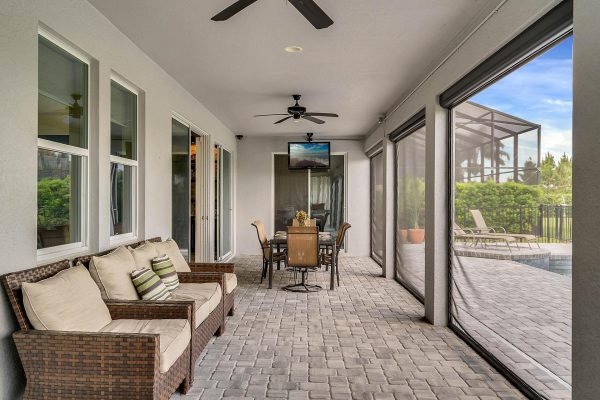 Covered lanai with seating area and dining table, overlooking a pool, featuring ceiling fan and television, part of a spacious Windermere lakefront home.