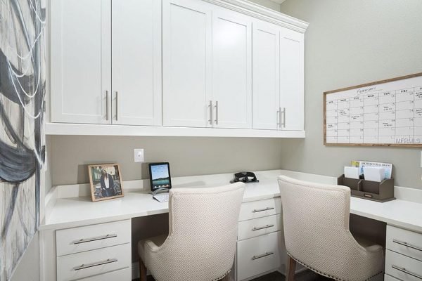 Home office with white cabinetry, two chairs, a calendar, and a laptop on a desk, reflecting modern design suitable for remote work in the property listing at 1827 Hawksbill LN, Saint Cloud, FL.
