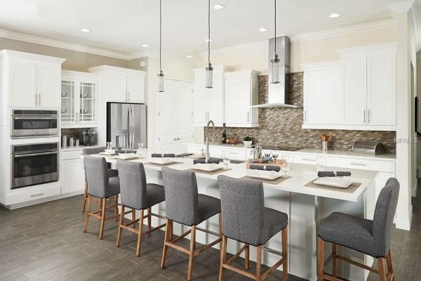 Modern kitchen with white cabinets, granite countertops, and stainless steel appliances, featuring an island with gray bar stools and stylish pendant lighting, designed for entertaining in the 1827 Hawksbill LN property, Saint Cloud, FL.