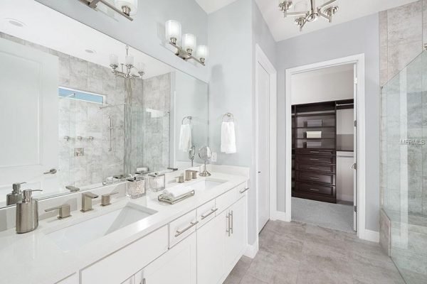 Luxurious bathroom featuring dual sinks, modern fixtures, and a spacious walk-in shower, with upgraded wall tile and a stylish design, part of the property at 1827 Hawksbill LN, Saint Cloud, FL.
