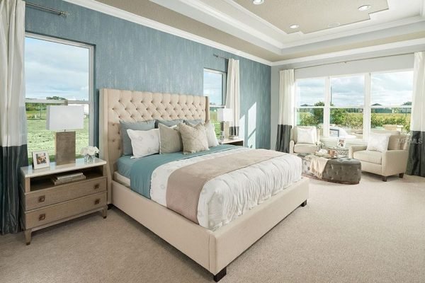 Spacious bedroom featuring a king-sized bed with a tufted headboard, decorative pillows, bedside tables, large windows with scenic views, and a cozy seating area, showcasing modern interior design elements.