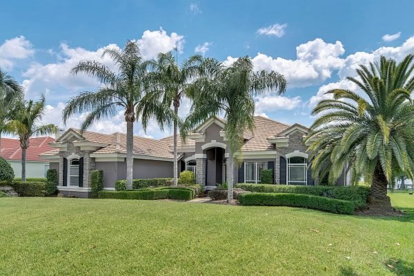 Exterior view of a luxurious single-family home at 2039 Water Key Drive in Windermere, FL, featuring palm trees, a manicured lawn, and a stone facade under a bright blue sky.