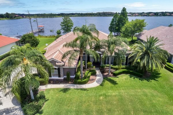 Lakefront home at 2039 Water Key Drive, Windermere, featuring lush landscaping, palm trees, and a view of Lake Roberts, highlighting the property's expansive outdoor space and waterfront accessibility.