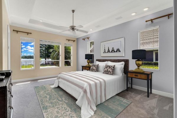 Master bedroom with lake views, featuring a king-sized bed, decorative pillows, two nightstands, large windows, and a ceiling fan, showcasing a serene and spacious atmosphere.