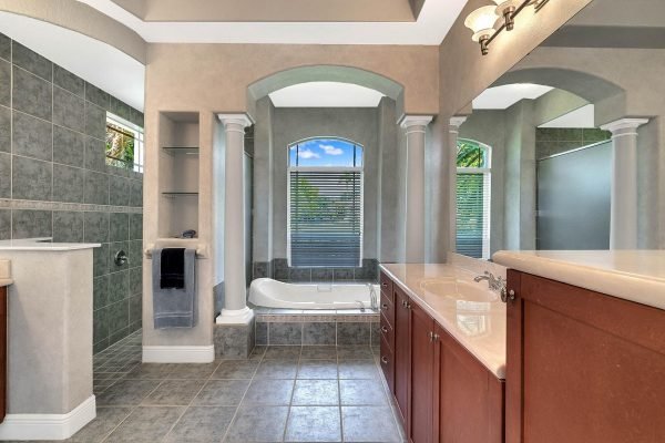 Luxurious bathroom featuring a freestanding tub, dual vanities, and elegant tile work, with natural light streaming through arched windows, in a lakefront home at 2039 Water Key Drive, Windermere, FL.