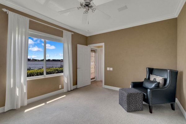 Bright bedroom with lake views, featuring a window with sheer curtains, a dark armchair, and a small ottoman, in a private lakefront home on Water Key Drive, Windermere, FL.