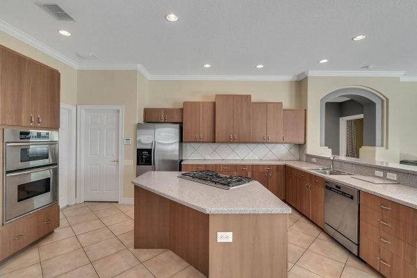Modern kitchen with wood cabinetry, stainless steel appliances, and a spacious island, showcasing an open floorplan ideal for entertaining in a lakefront home in Windermere, FL.