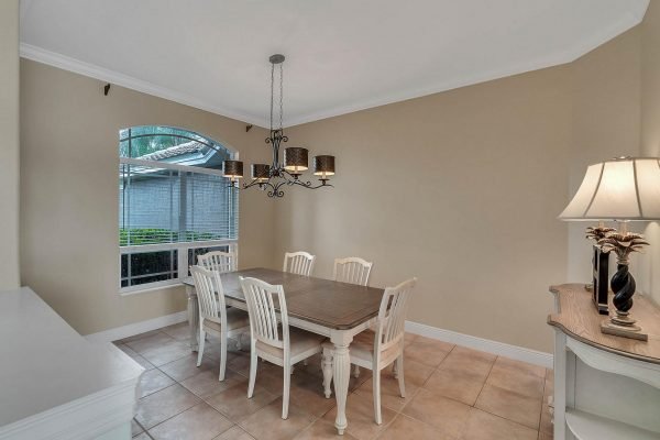 Dining area featuring a wooden table with six white chairs, elegant chandelier, and large window providing natural light, in a lakefront home at 2039 Water Key Drive, Windermere, FL.